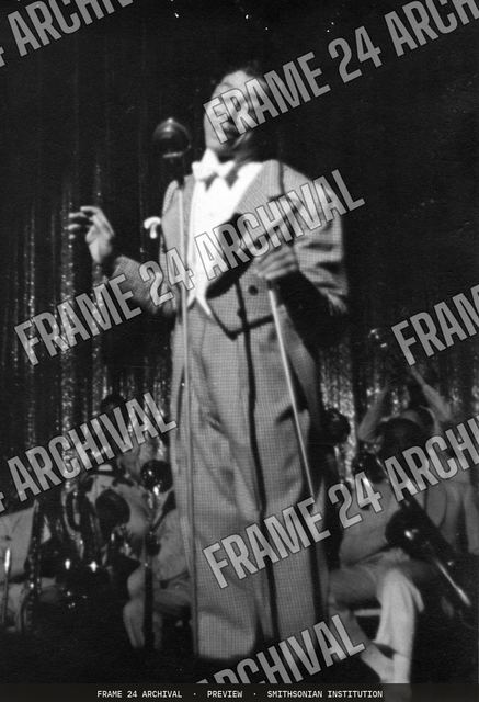 Print of Cab Calloway in checked suit standing in front of microphone, vintage black and white photograph